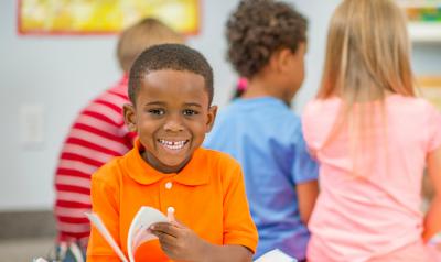 A young boy smiling and reading a book