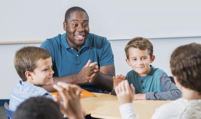 Young black male teacher of color sites at a table with group of white boys.