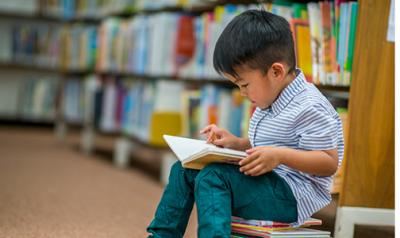 Preschool boy reading a book in the library