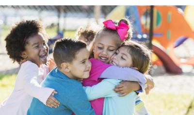 A group of diverse young children hugging on a playground