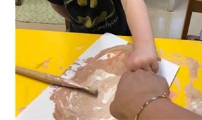 A child and teacher mixing brown paint together to match skin tones.