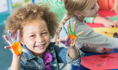 preschooler holds up hands covered in finger paint