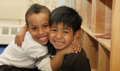 Two young boys of color embrace and small into the camera.