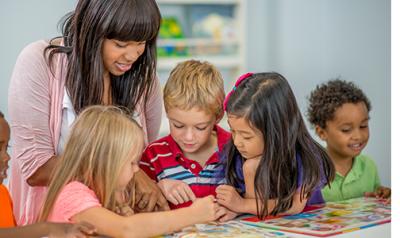 A teacher showing children a picture on a table.