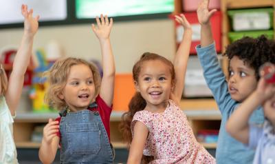 Children raise their hands to engage in a circle time discussion. 