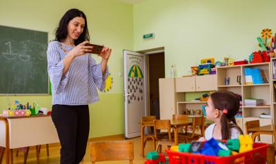 A teacher using a device to document a child playing in the classroom.