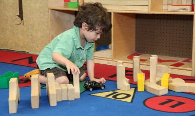 Preschool boy playing with blocks and a toy car on the floor 