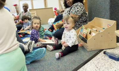 Toddlers playing in a classroom on the floor, sitting with three teachers