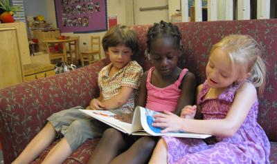 three preschoolers in a classroom sitting on a chair reading a book