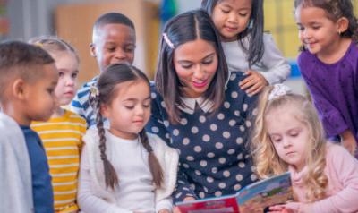 teacher with children gathered around a book