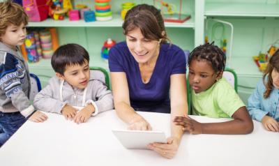 children looking at a tablet with a teacher