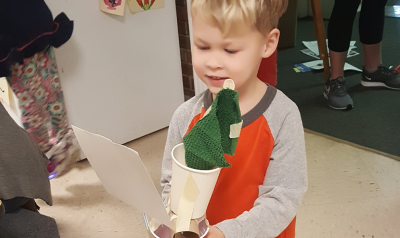 A child holds a sail car created from open-ended materials.