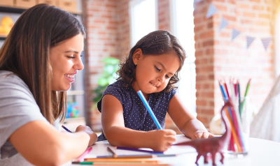 A teacher overseeing a child drawing to illustrate a story.