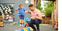 Teacher helps a boy jump over buckets on a playground