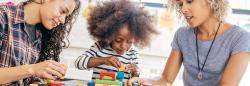 Two women and a young girl sitting at a table and playing with blocks