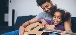Father and daughter playing guitar on couch
