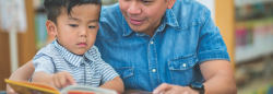 Male teacher and preschool student reading a book