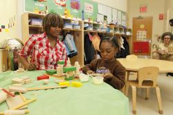 An African-American educator interacts with a young African-American girl at a low table with blocks.