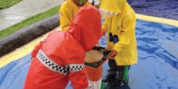 children in raincoats playing outdoors with a traffic cone