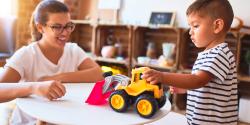 A teacher interacting with a child playing with a truck toy.