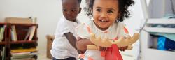 Toddler girl laughing and riding on a pony toy while toddler boy holds on