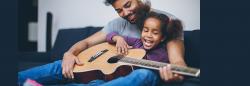 Father and daughter playing guitar on couch