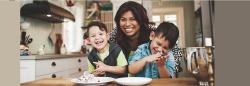 Mother hugging two sons in the kitchen that are sitting in her lap 