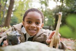 Boy playing outdoors with toy dinosaur