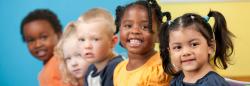 Young children in a line smile for a photograph. 