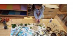 a child working on a craft project with grass, sticks, and sand