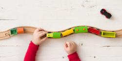 A child's hands can be seen guiding a toy train down a wooden track