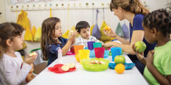 Children eat food at a table with their teacher.