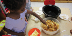 A child stirs food at the cooking table.