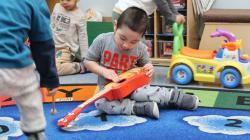 A young child playing with a guitar in a classroom