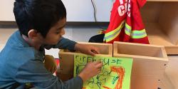 A young boy in a classroom taping an image to block. 