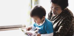 Preschool boy in his grandma's lap, learning on a tablet