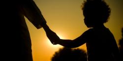 A child and a family member in silhouette against a setting sun.