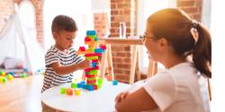 A young boy plays with some blocks while a teacher observes.