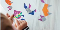 A young child copies designs of various geometric shapes on a piece of paper.