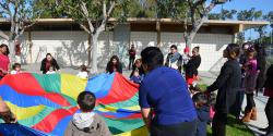 articles on urban education A group of children and their parents play with a rainbow-colored parachute.