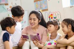 a teacher reading a book surrounded by children