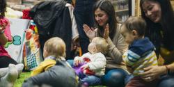 Infants and their parents sit in a circle clapping and singing together