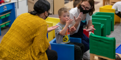 two teachers in face masks making hand gestures with a child