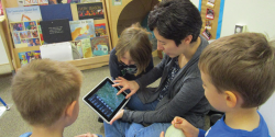 a teacher showing children a game on an ipad