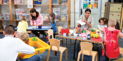 a classroom with multiple tables with children and teachers