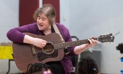 An educator playing the guitar and singing to students