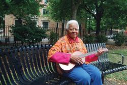 Ella Jenkins sitting on a bench with a guitar in her hands