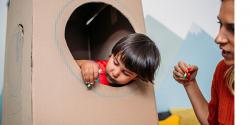 student playing in a cardboard fort with teacher