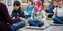 Students sits on mats and do meditation exercises with a teacher 