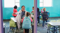 A teacher welcoming her students into the classroom.